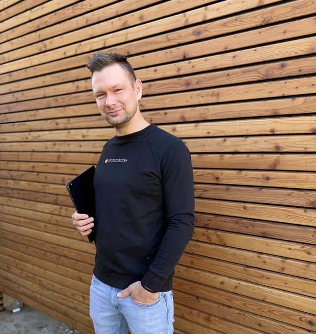Patrick Weiß, Kfz-Meister und persönlicher Ansprechpartner, mit Tablet vor einer Holzwand