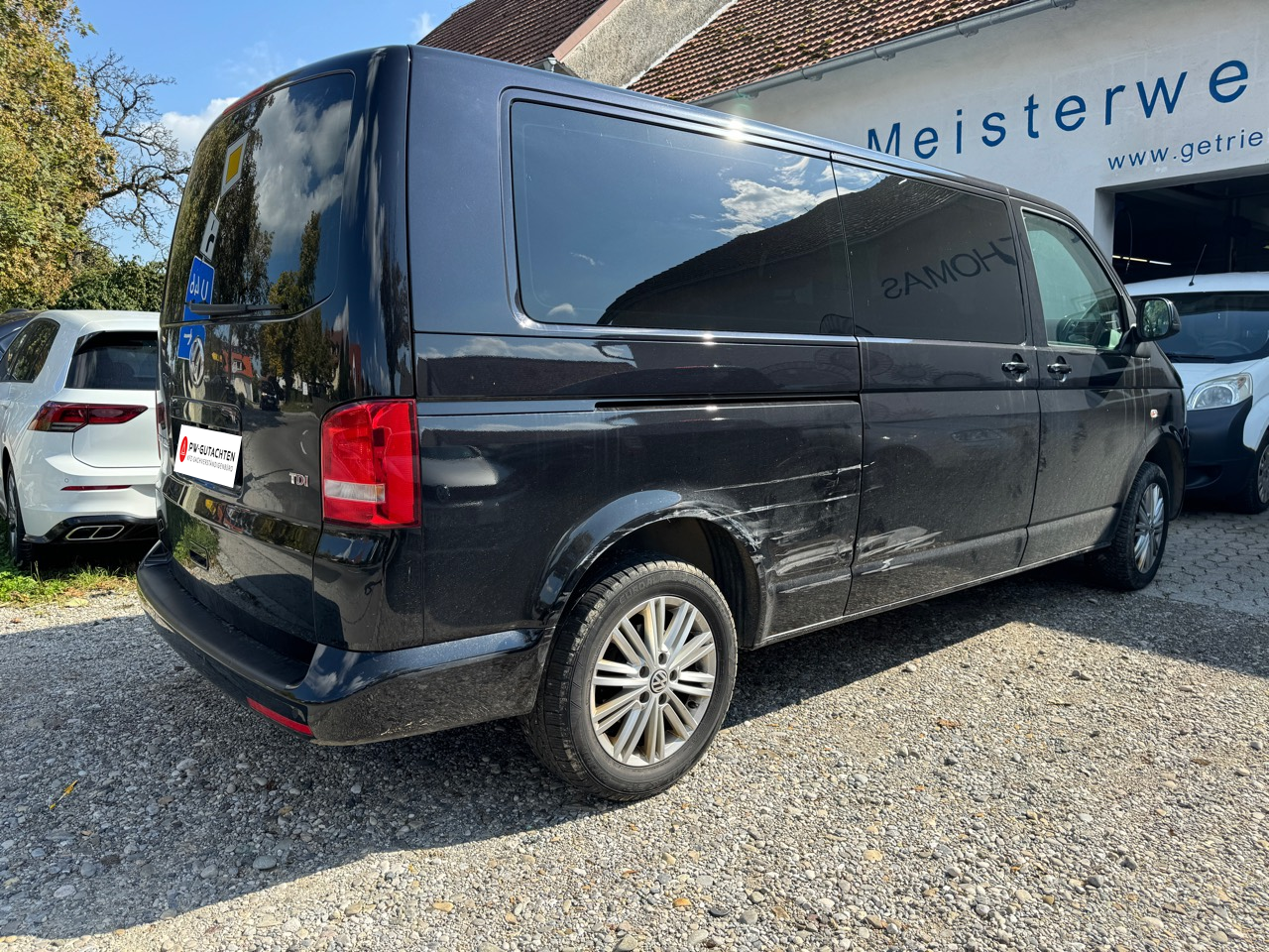 Schräge Heckansicht des VW Caravelle mit Seitenschaden und PW-Gutachten-Logo anstelle des Kennzeichens